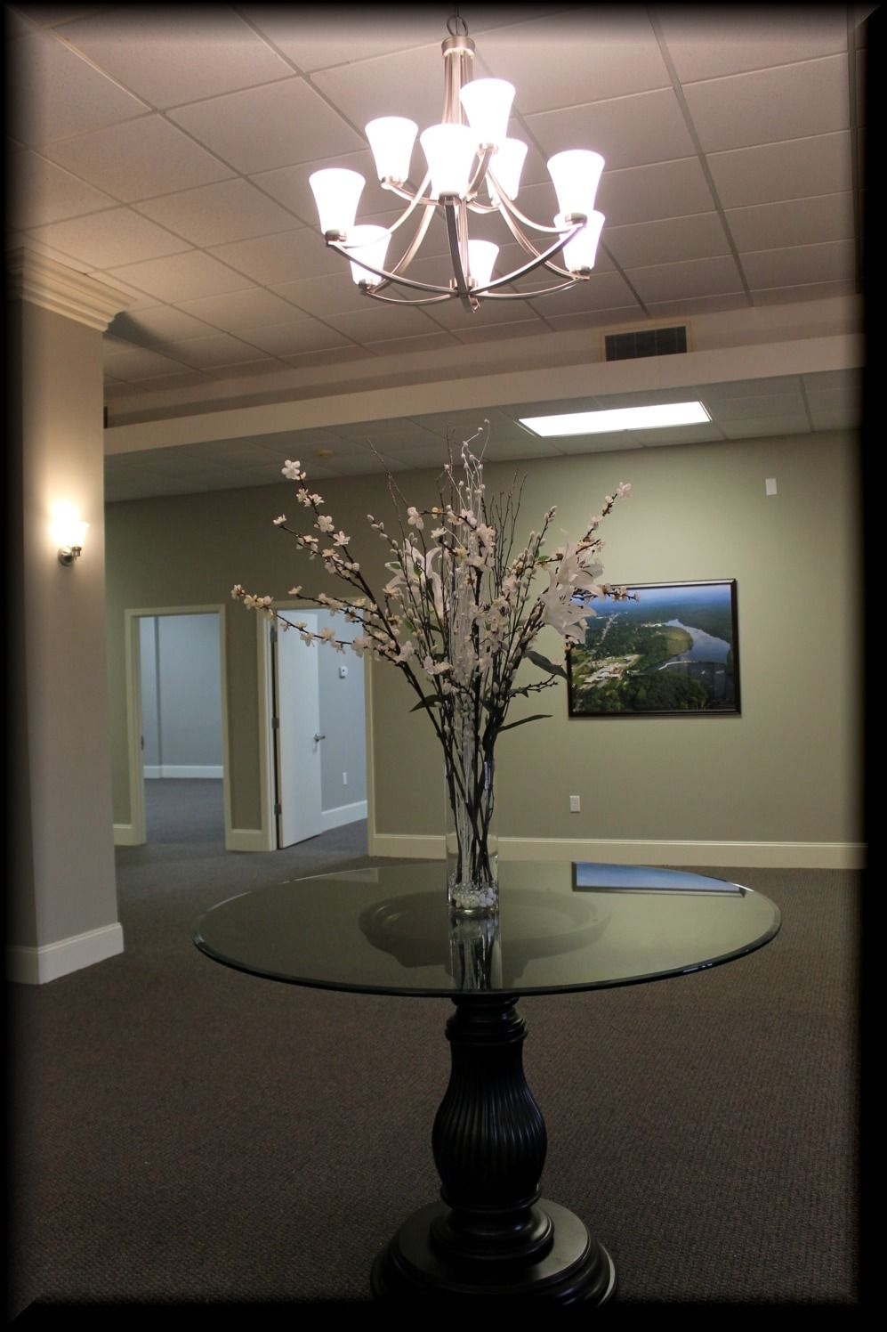 An entryway with a chandelier, round table with floral arrangement, and a landscape photo.