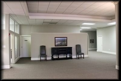 Empty, gray-carpeted room with a console table, two chairs, and a landscape painting. White ceiling and walls.