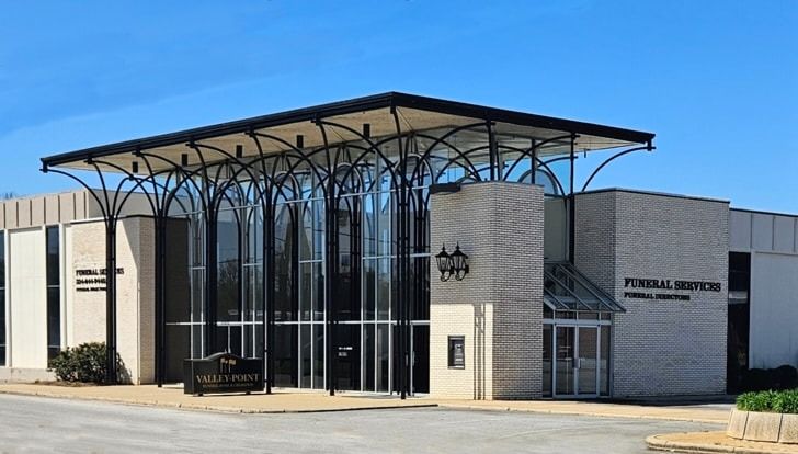 Funeral home with a white brick facade and a canopy supported by arched, black metal supports; blue sky.