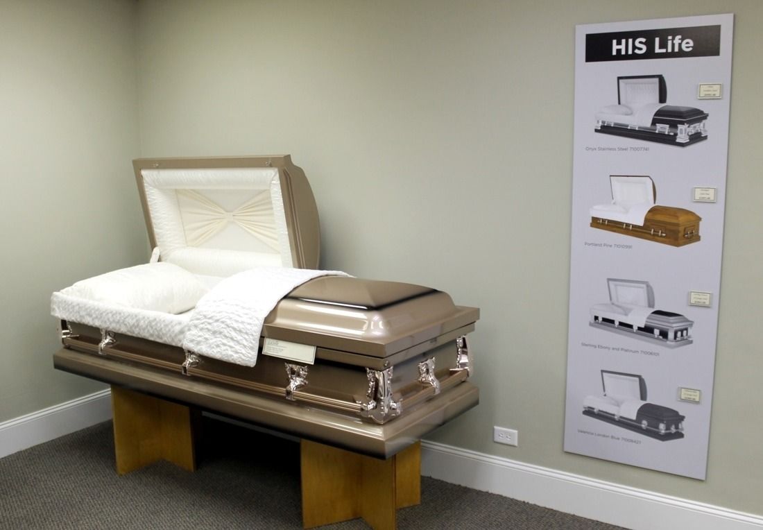 Brown casket on display in a funeral home showroom, with a product display board.
