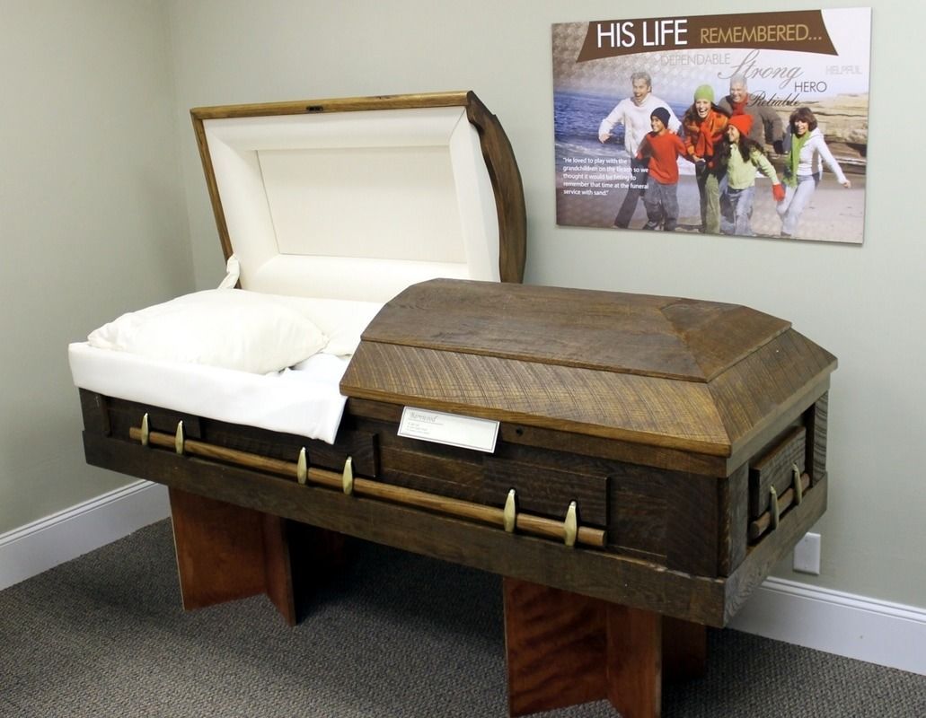 Wooden casket with partially open lid, on a stand, against a wall with a family photo.