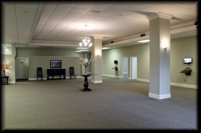 Empty, spacious room with columns, carpet, and a chandelier; possibly a reception or event space.