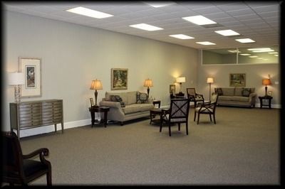 Spacious waiting room with neutral colors, couches, chairs, lamps, artwork, and a tiled ceiling.