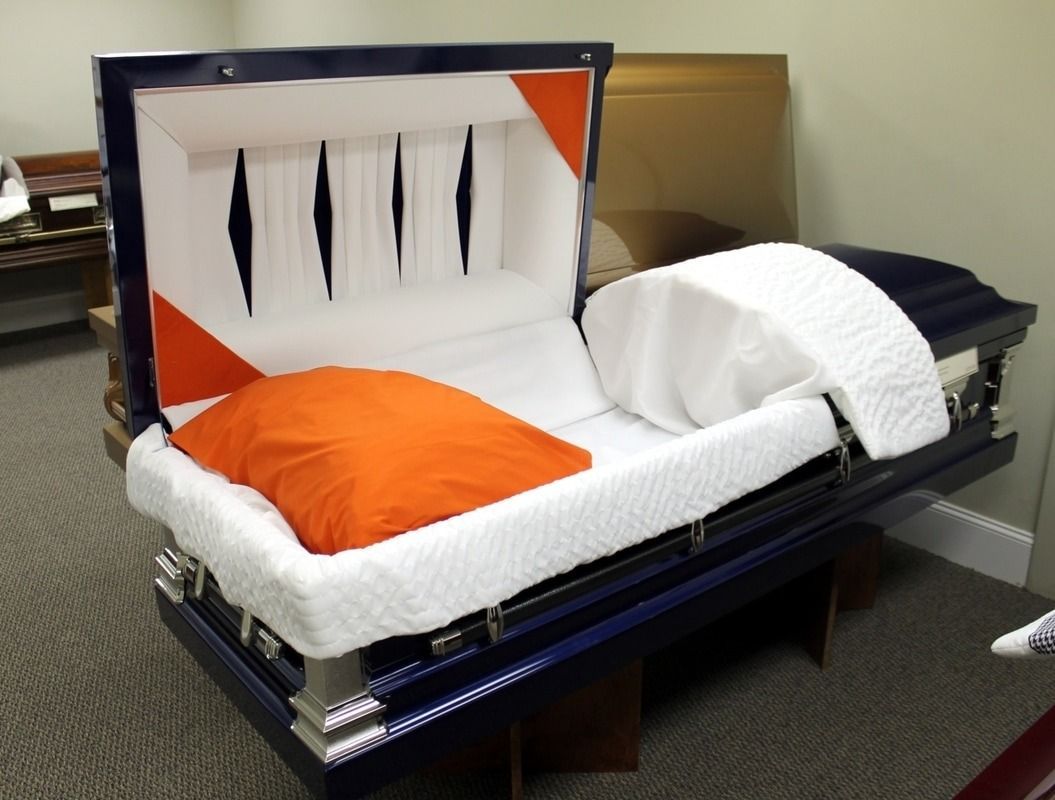 Blue and white casket with an open lid, orange pillow, white bedding.