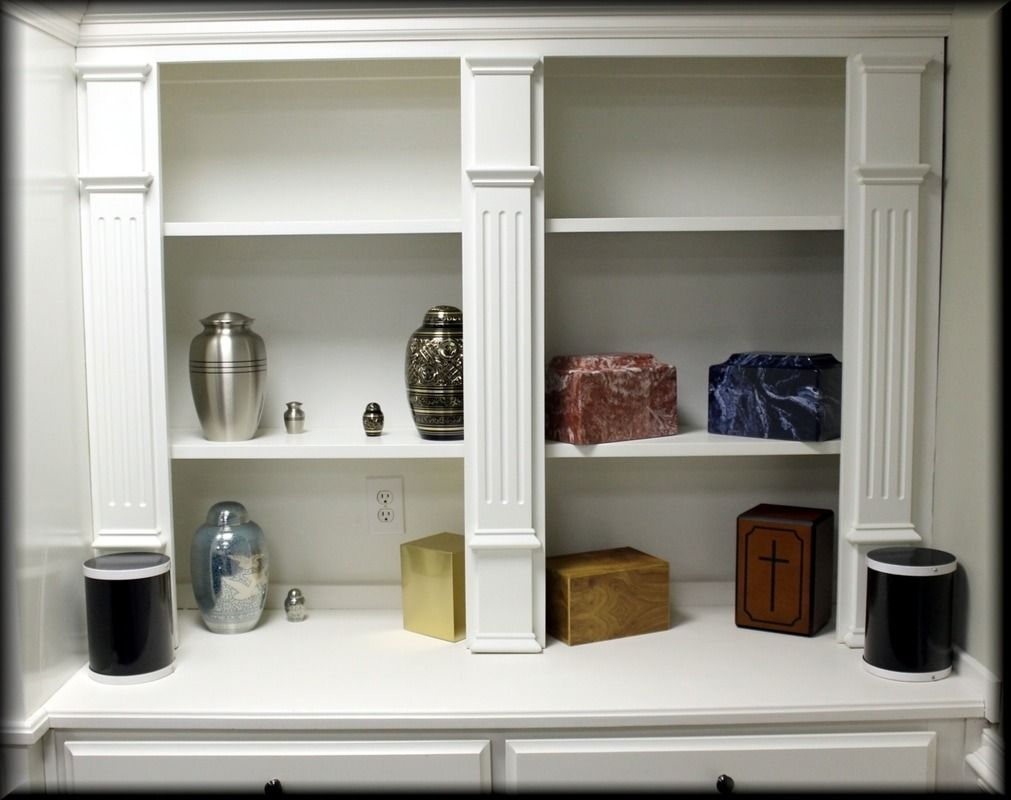 White built-in shelving unit displaying various cremation urns and containers.