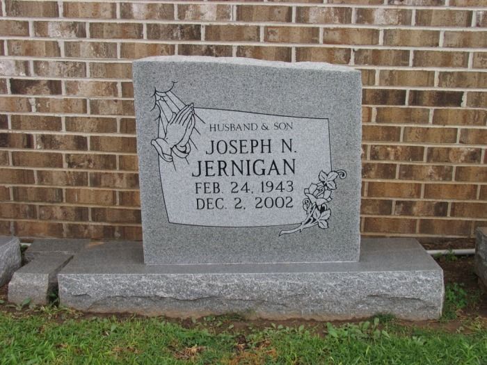Gravestone of Joseph N. Jernigan, with dates Feb 24, 1943 - Dec 2, 2002, against a brick wall.