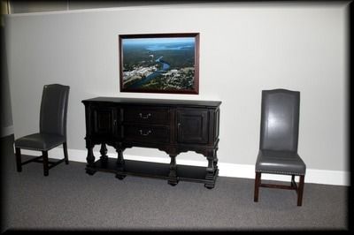 Dark wood buffet with picture and two gray chairs on a gray carpet.