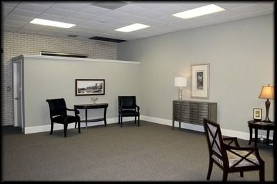 Gray-walled waiting room with chairs, side tables, artwork, and a white ceiling with recessed lights.