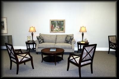 Living room with a sofa, chairs, coffee table, lamps, and artwork; neutral colors.