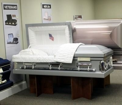 Gray open casket with white interior and American flag, on display in a funeral home.
