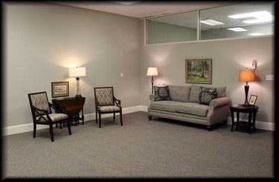 Waiting room with neutral walls, gray carpet, and seating: sofa, chairs, and side tables with lamps.