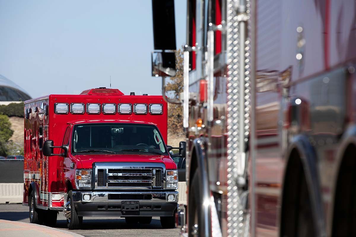 Red ambulance and fire truck parked on a sunny road.