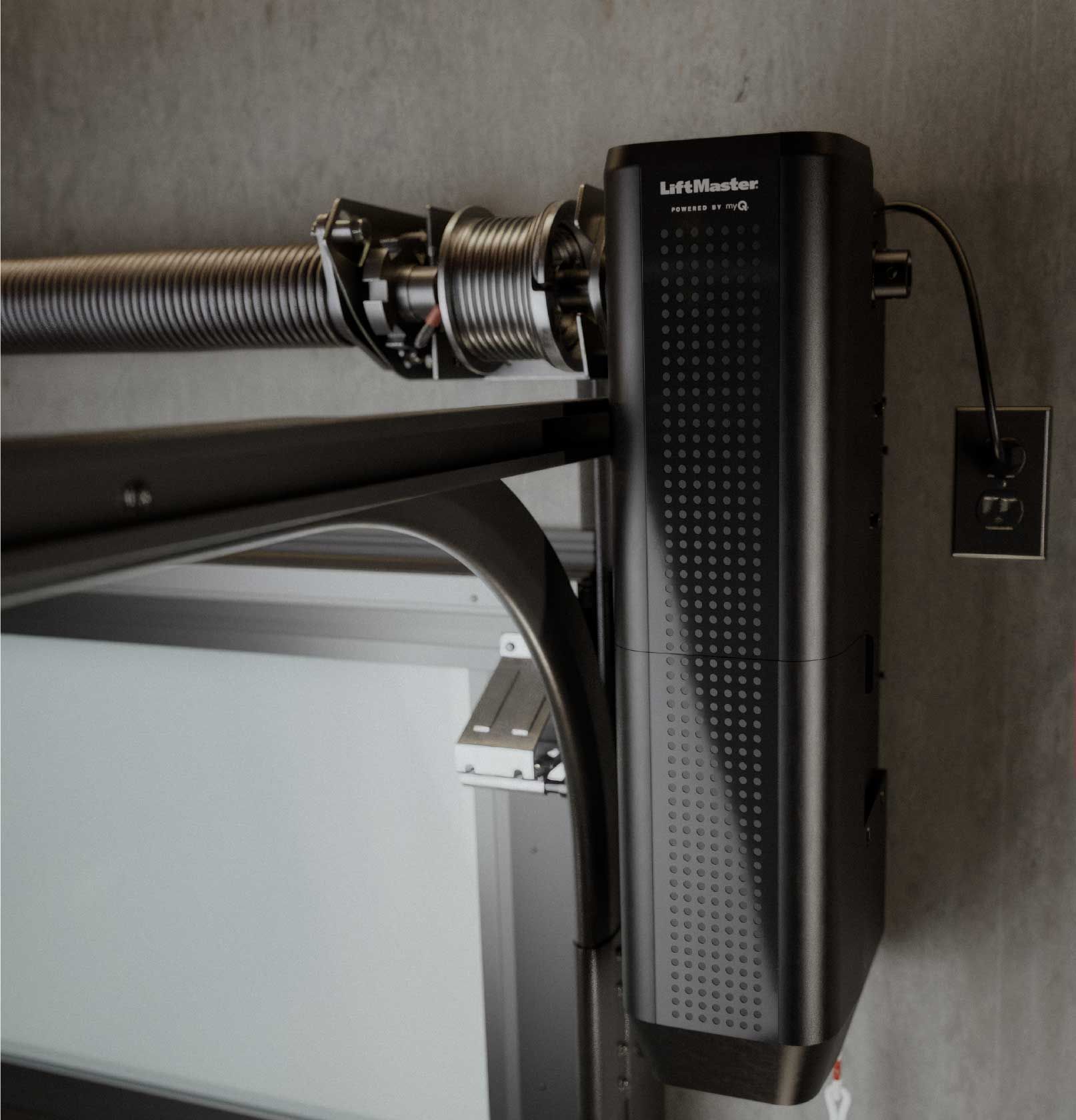 Garage door opener mounted on the ceiling, connected to the door track. Black and white, indoors.