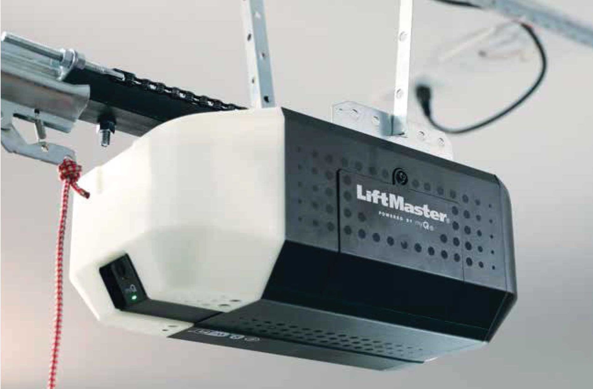 Garage door opener mounted on the ceiling, connected to the door track. Black and white, indoors.