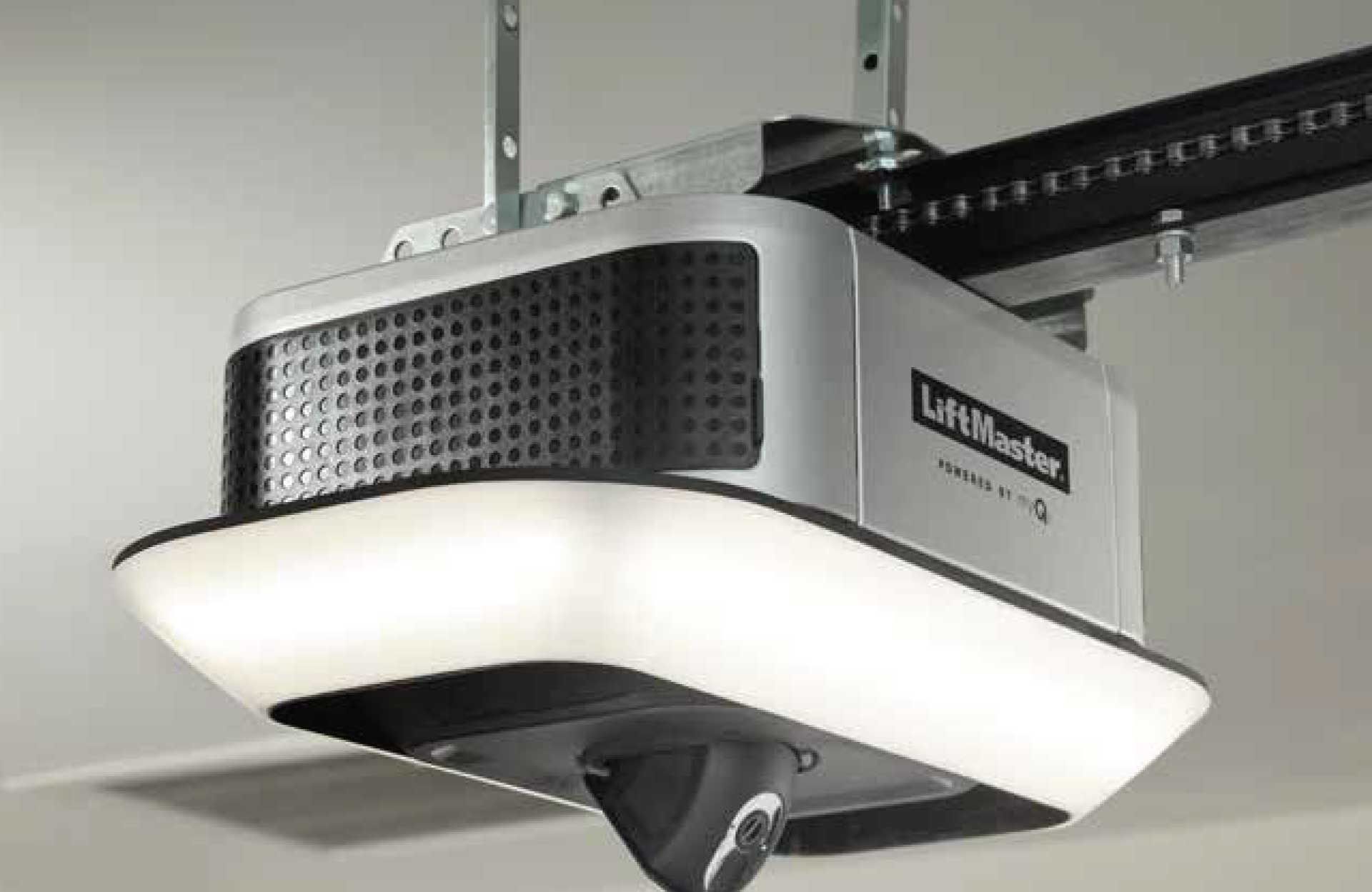 Garage door opener mounted on the ceiling, connected to the door track. Black and white, indoors.