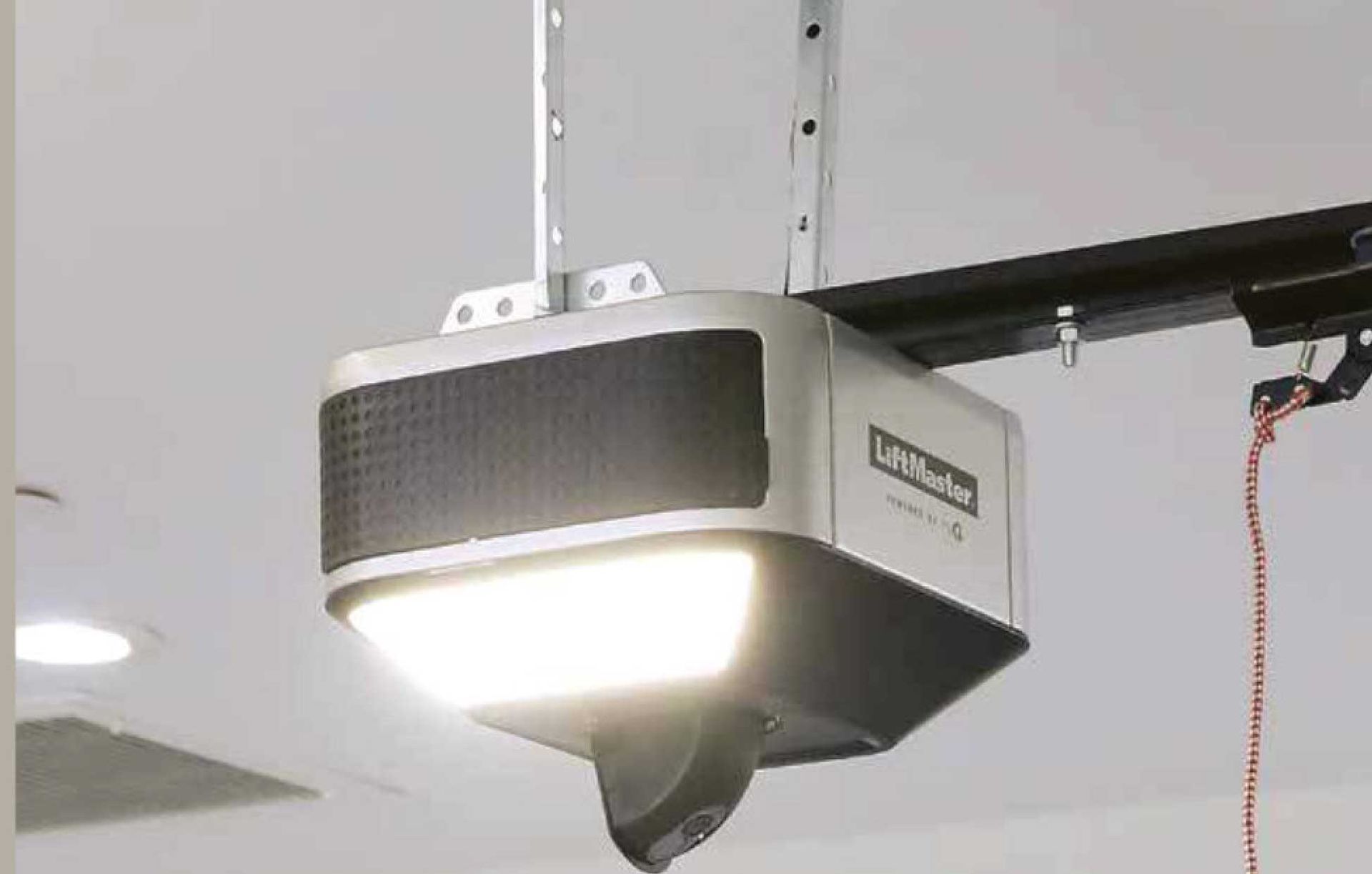 Garage door opener mounted on the ceiling, connected to the door track. Black and white, indoors.