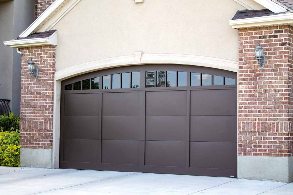 Three beige garage doors with small windows, flanked by stone columns and a metal roof.
