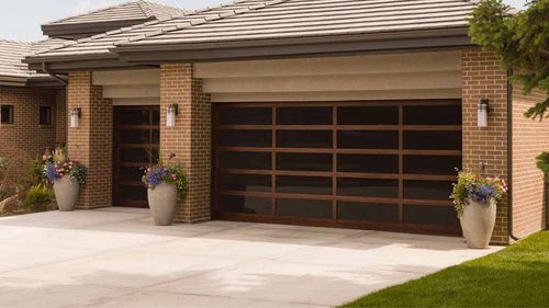 Modern two-story house with black garage doors and wooden siding. White exterior with large windows, green lawn.