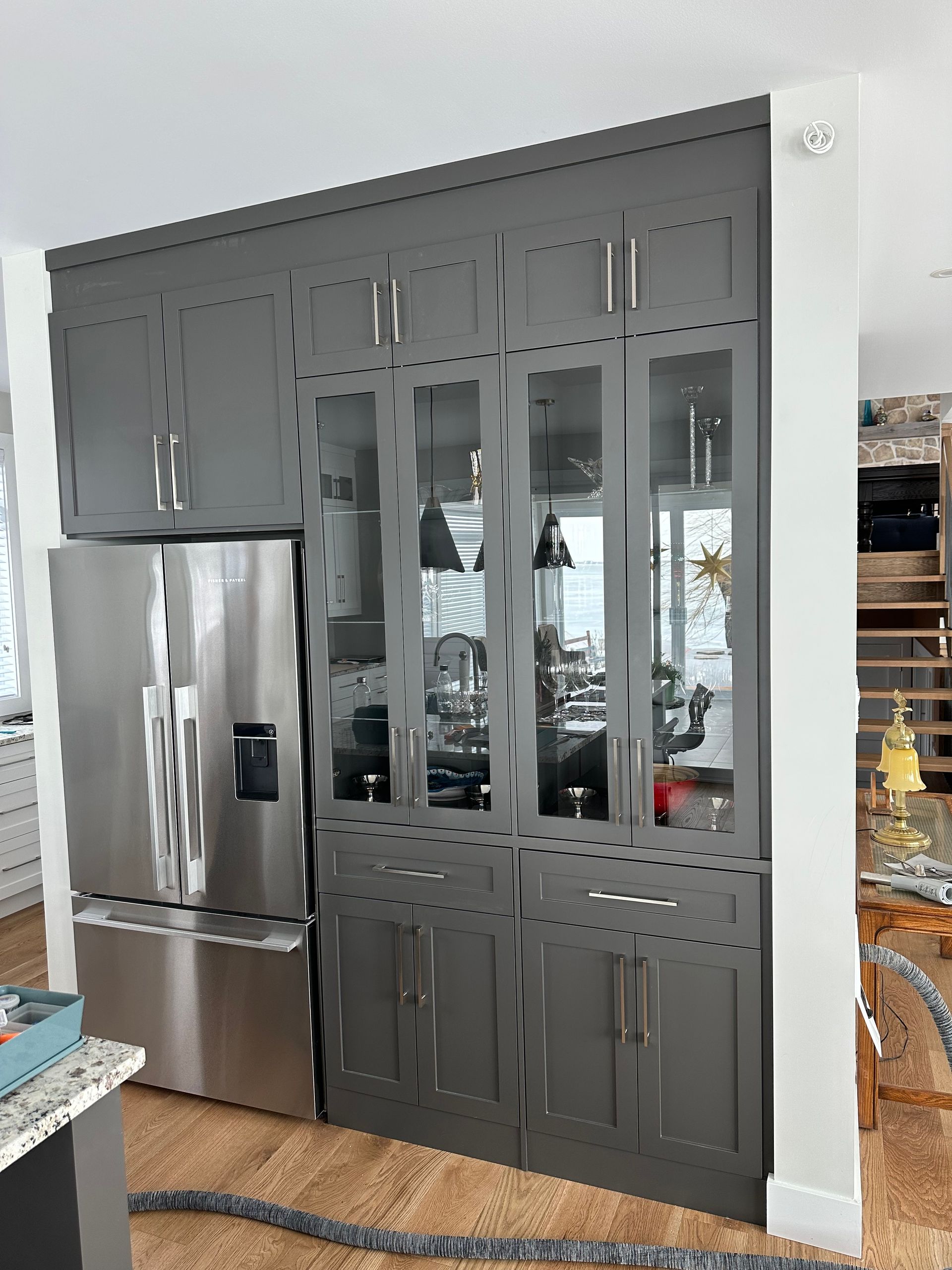 Des armoires de cuisine grises avec portes vitrées, un réfrigérateur en acier inoxydable et une quincaillerie moderne.