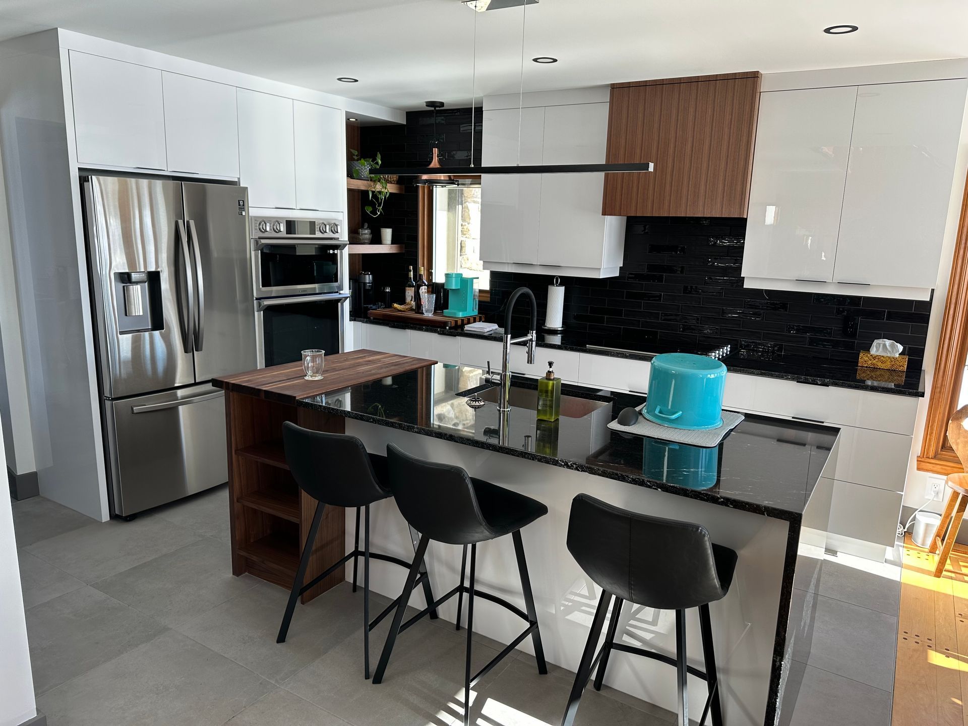 Cuisine moderne avec îlot central noir, placards blancs, appareils électroménagers en acier inoxydable et trois tabourets de bar noirs.