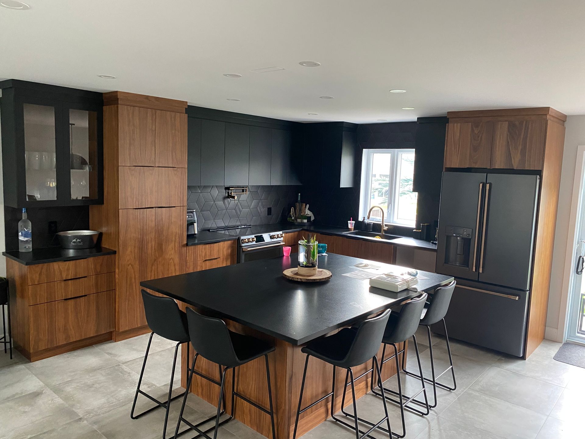 Cuisine moderne avec placards noirs et en bois, îlot central avec tabourets et appareils électroménagers en acier inoxydable.