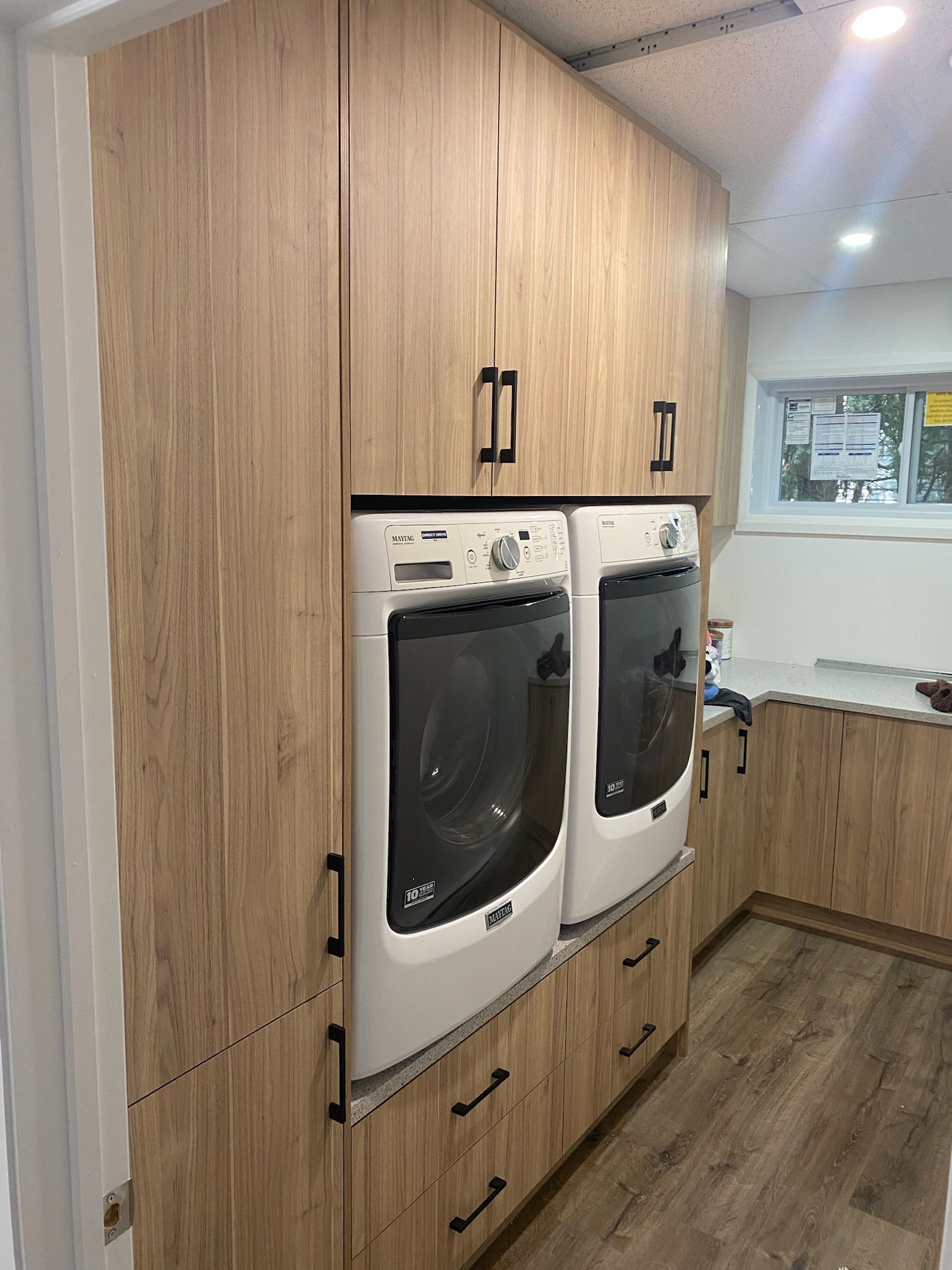 Buanderie avec des placards imitation bois entourant une machine à laver et un sèche-linge, et des tiroirs en dessous.