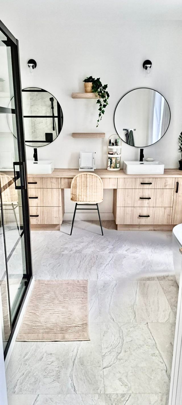 Salle de bains avec double vasque, miroirs ronds, meuble-lavabo en bois et chaise. Murs blancs et sol en marbre.