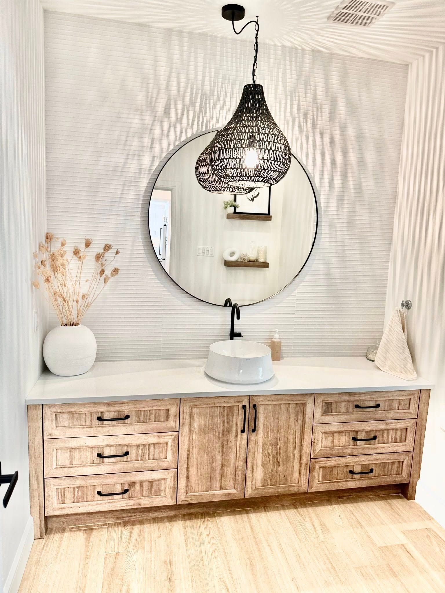 Salle d'eau avec meuble-lavabo en bois, miroir rond, mur texturé et suspension lumineuse.