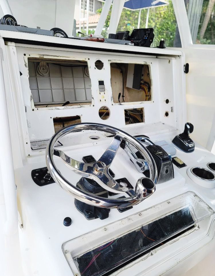 Boat helm with chrome steering wheel and exposed dashboard wiring, in an unfinished cockpit.