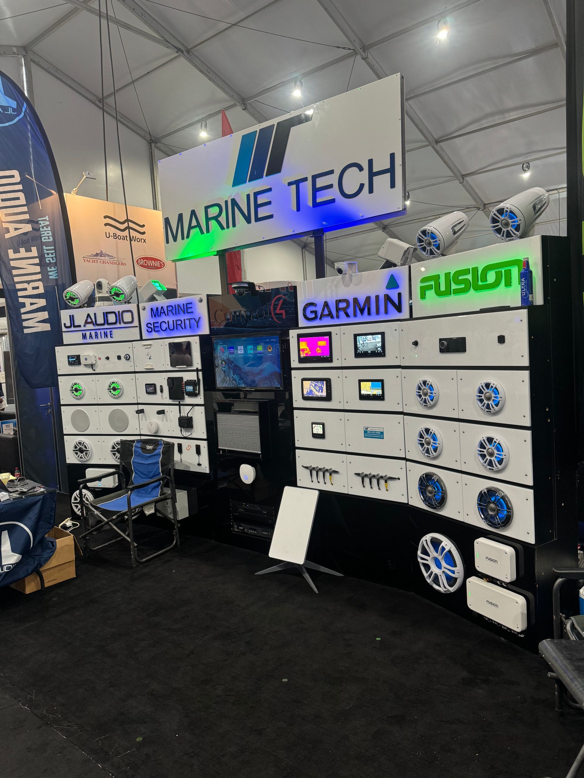 Marine Tech booth at a trade show displays marine audio and electronics. Products include Garmin, Fusion, and speakers.