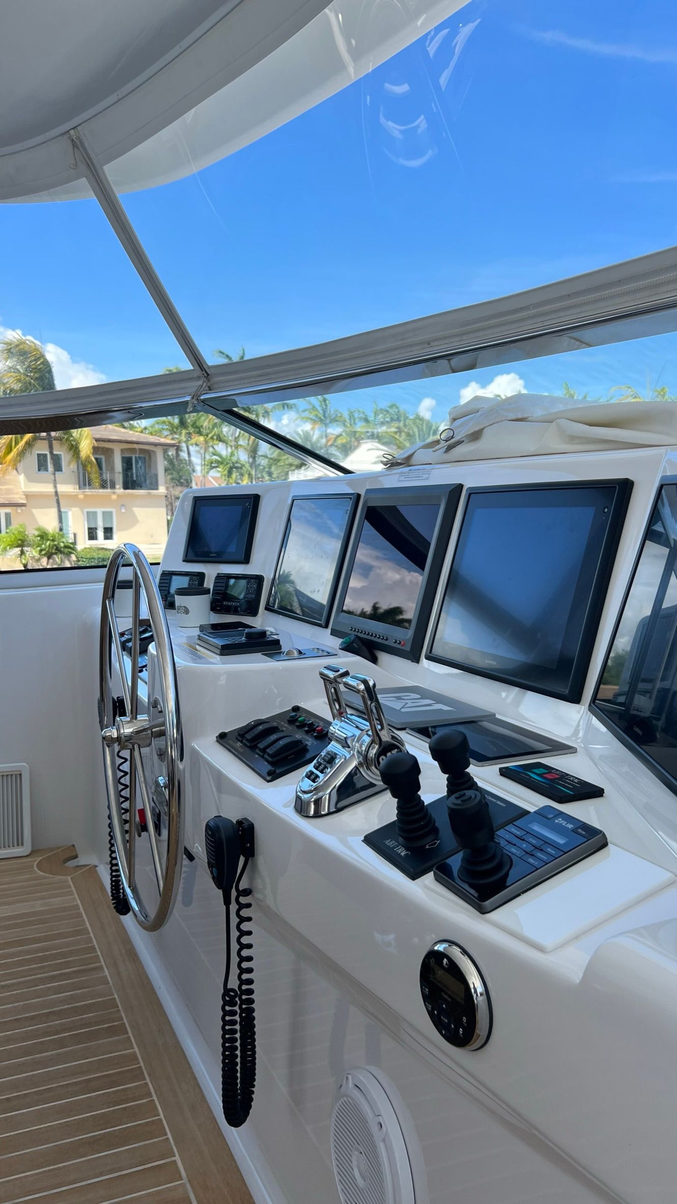 Boat dashboard with navigation screens, steering wheel, and controls, on a sunny day.