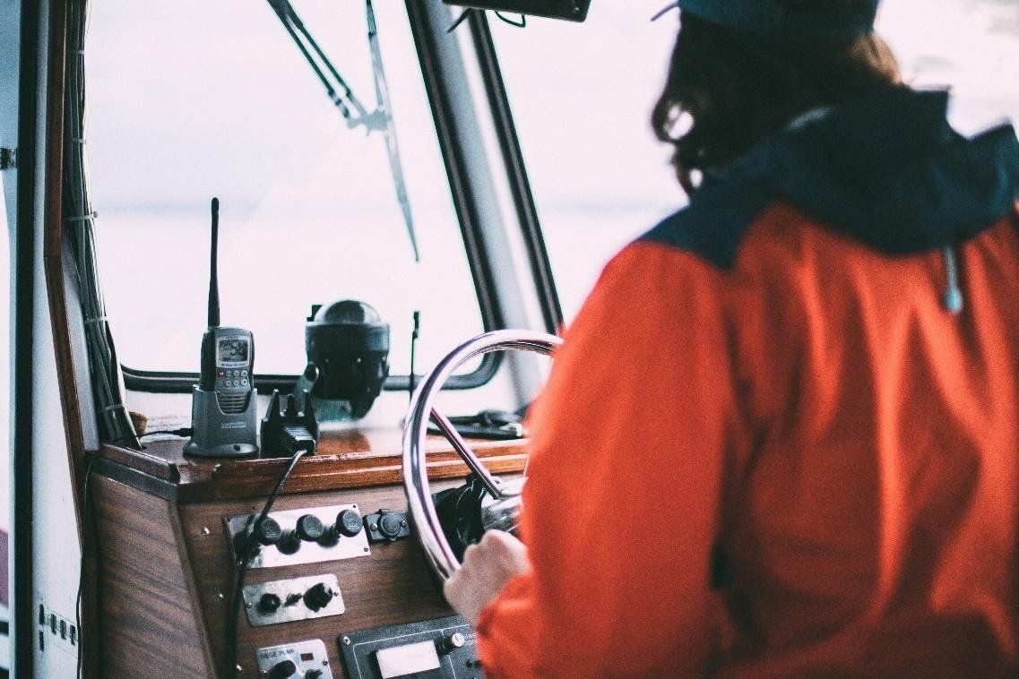 A man in an orange jacket is driving a boat.