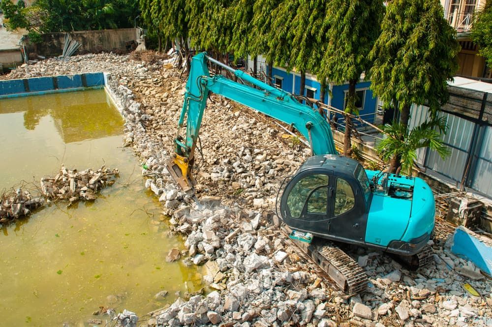 A Blue Excavator Is Destroying a Swimming Pool — Greenline Recycling in Ormeau, QLD