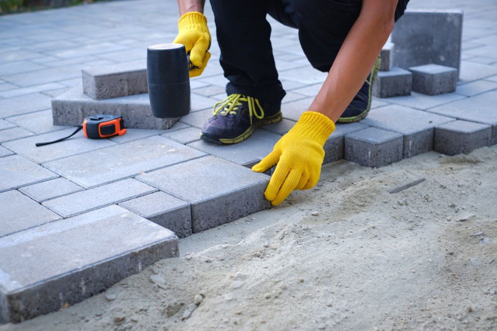 A Man Wearing Yellow Gloves Is Laying Bricks on A Sidewalk — Greenline Recycling in Redland Bay, QLD