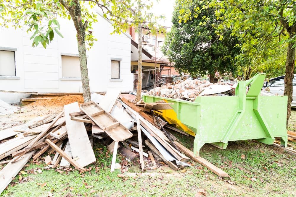A Green Dumpster Is Sitting Next to A Pile of Wood in Front of A House — Greenline Recycling in Brisbane, QLD