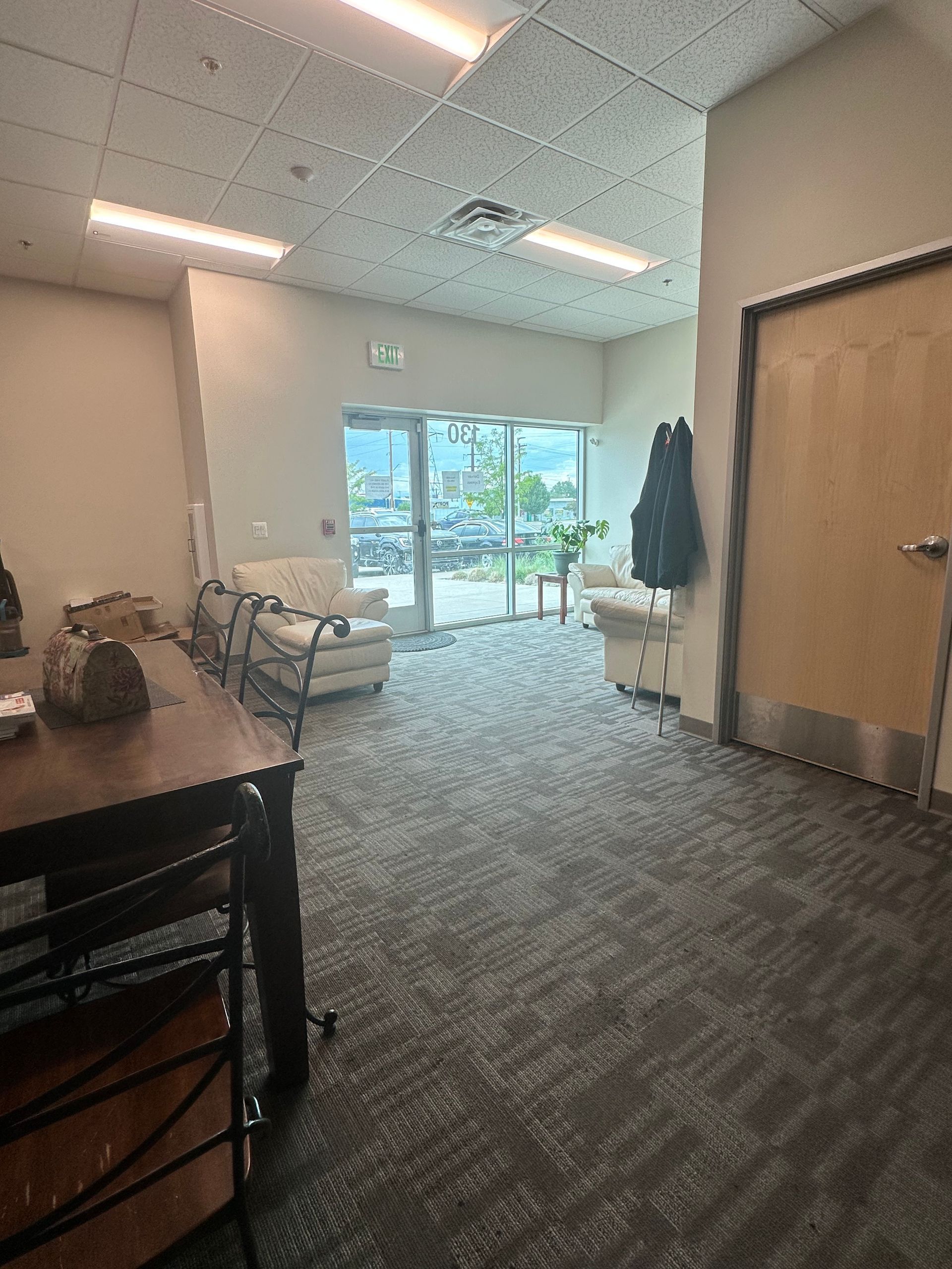 An empty office interior with a waiting area, carpet flooring, and glass doors leading outside.