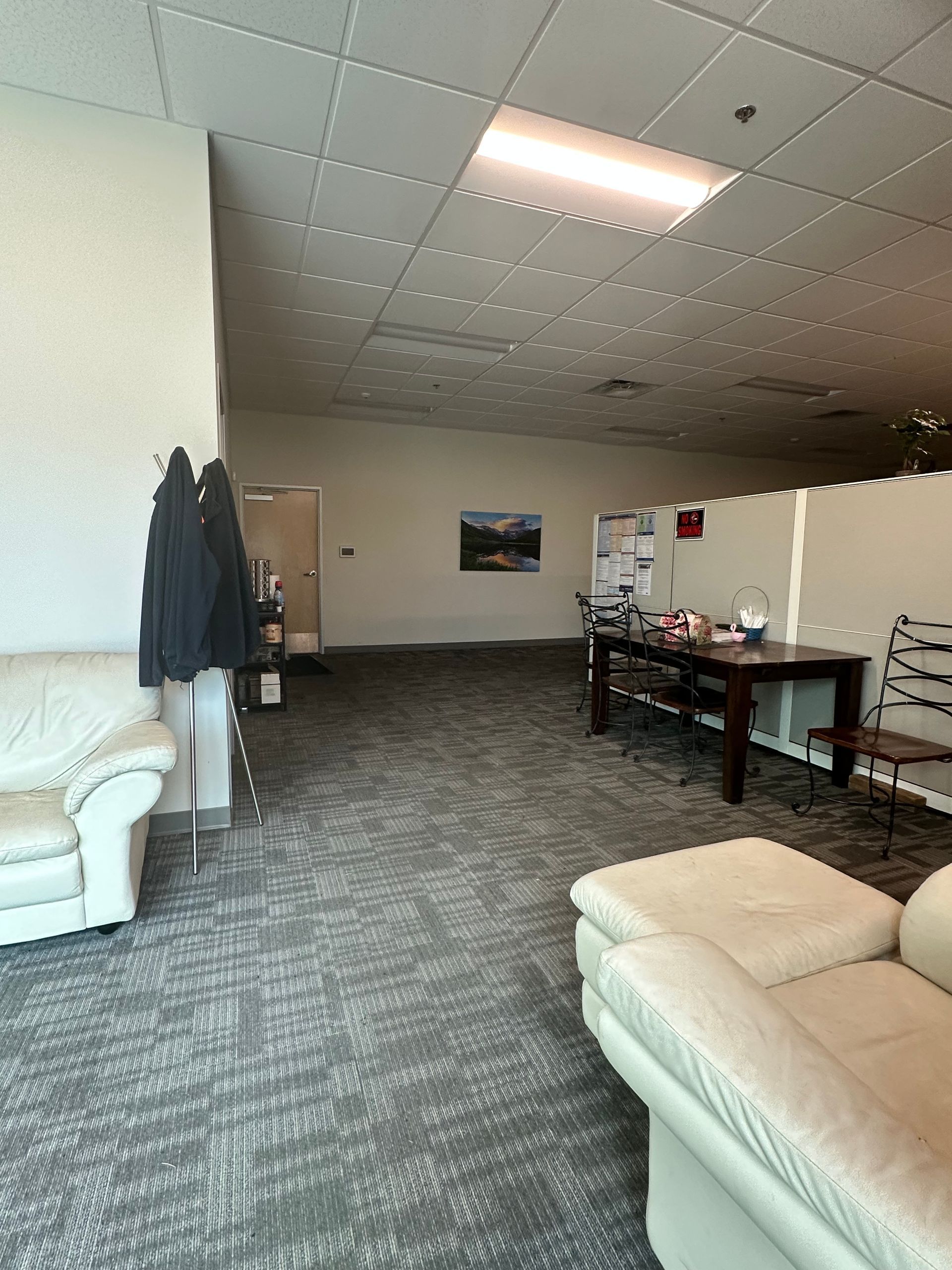 An empty office space with couches, a table, and cubicles. The carpet is gray.