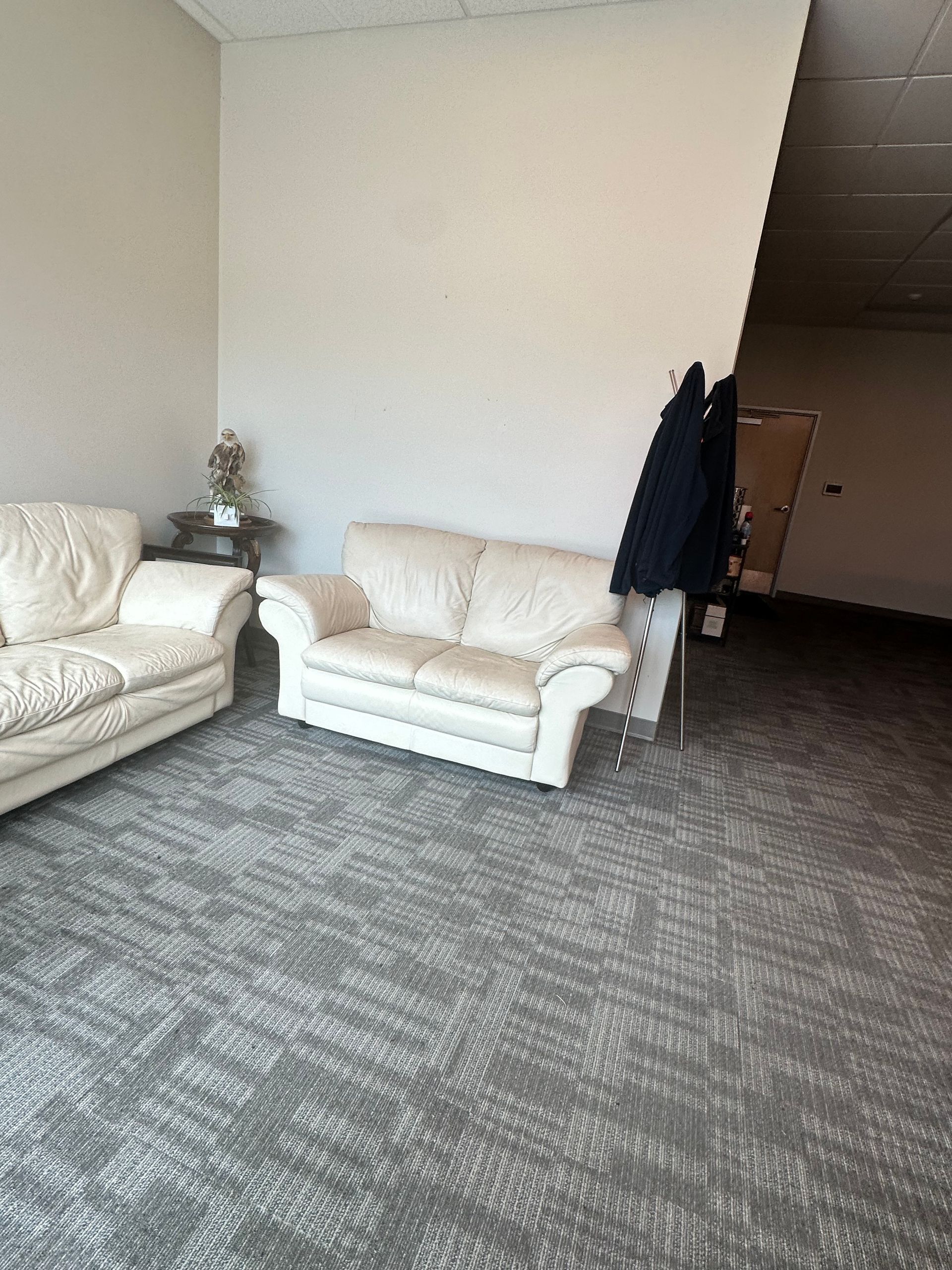 Two off-white sofas in a waiting area with gray patterned carpet and a coat rack.