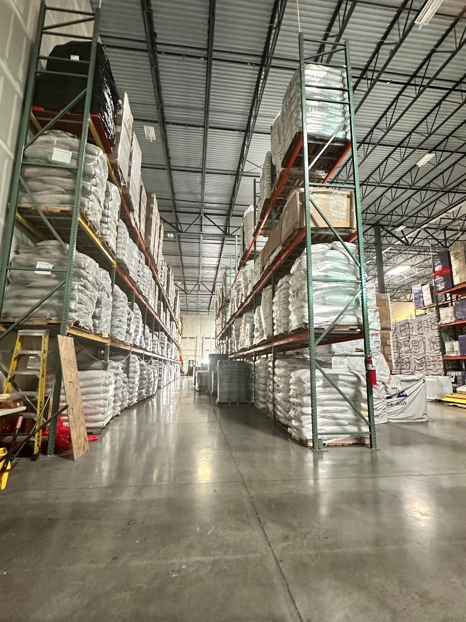 Warehouse interior with tall shelving packed with bags, boxes; concrete floor.