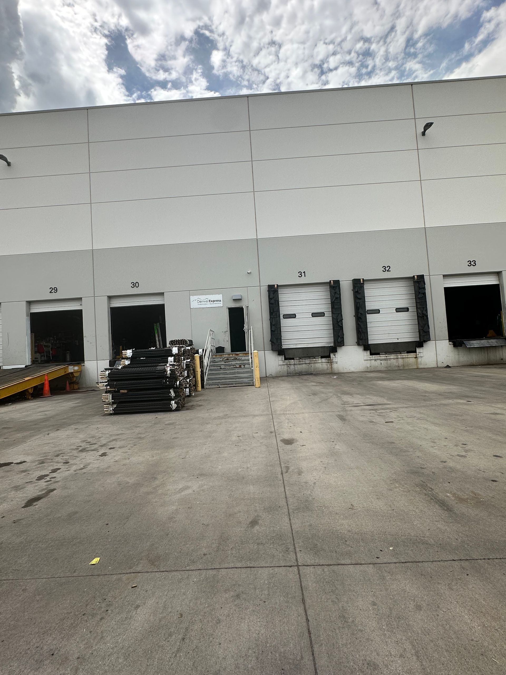Loading docks on a gray warehouse building, with open doors, gray concrete, and a cloudy sky.