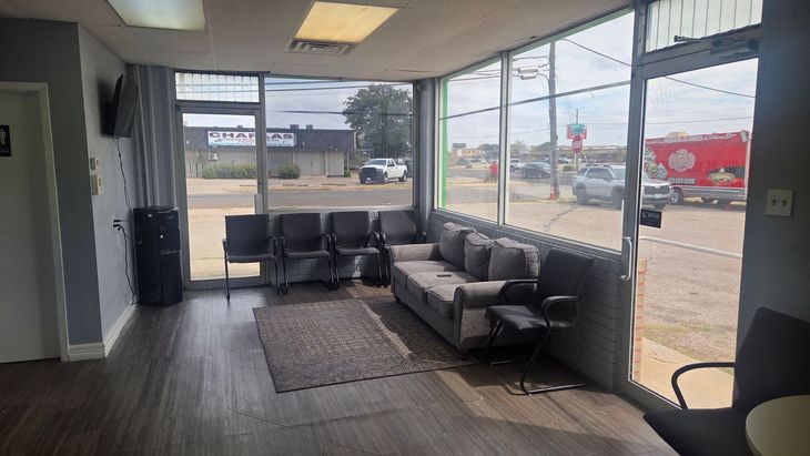 Empty office lobby with black chairs, gray sofa, and large front windows facing the street.