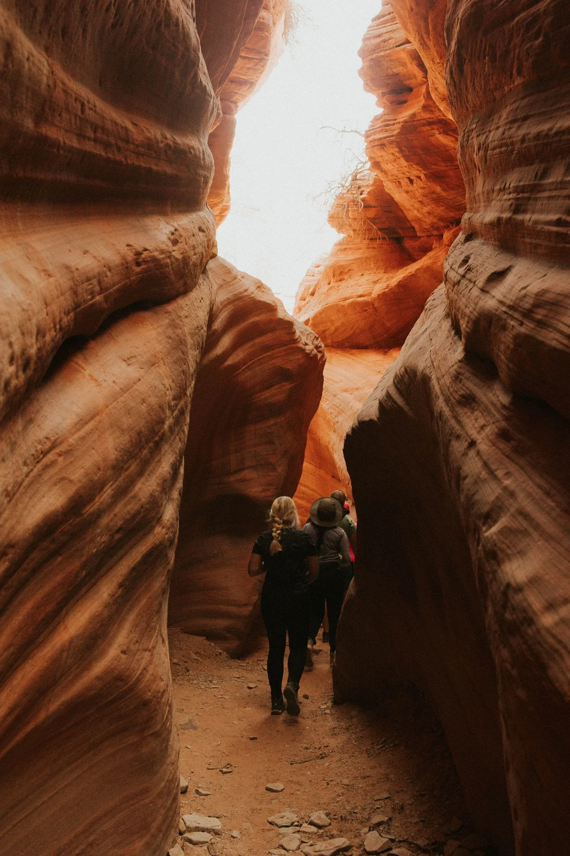 Hiker walking through a narrow red sandstone canyon with towering rock walls
