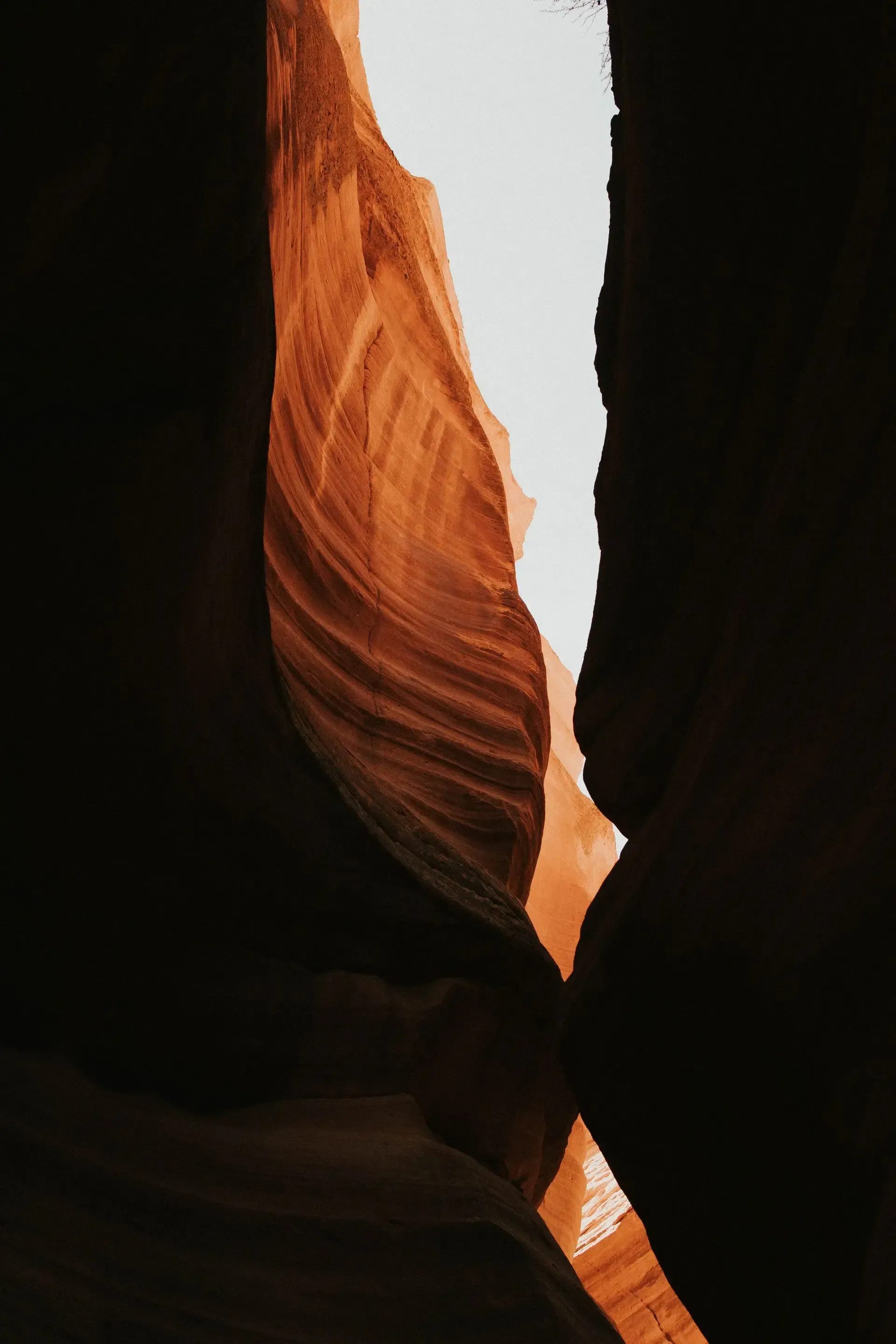 Narrow sandstone canyon with orange and brown layers, lit by sunlight from above.