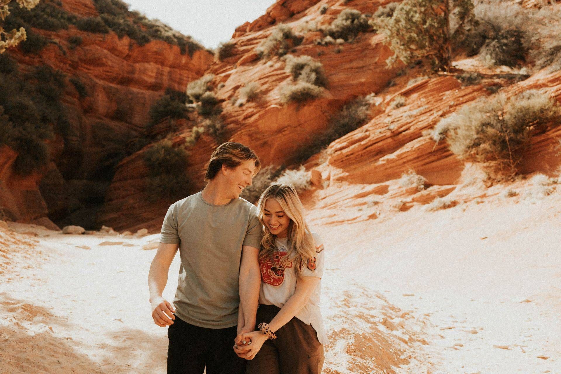 Two people walking together in a red rock canyon, smiling in warm sunlight.