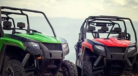 Two off-road ATVs, one green and one red, parked side by side on a rugged mountain overlook.
