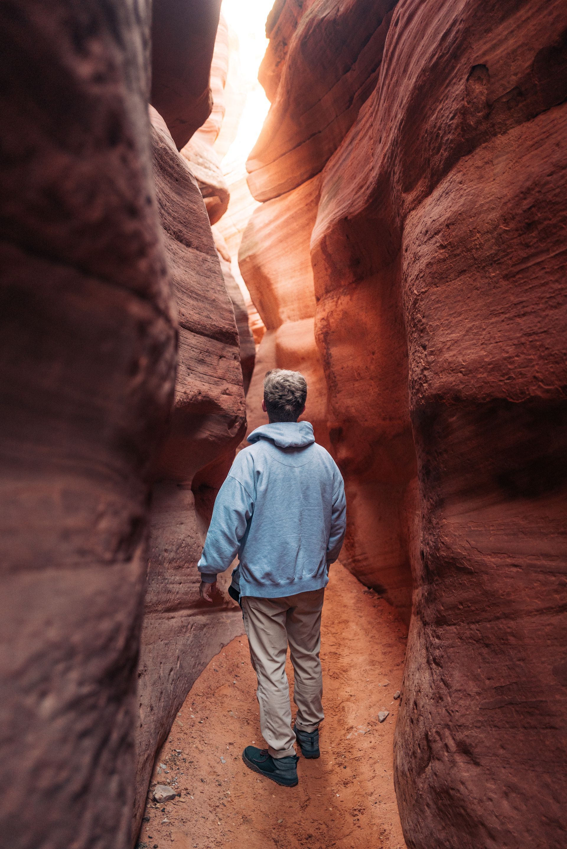 Person in blue jacket walking through a narrow, red-rock canyon.