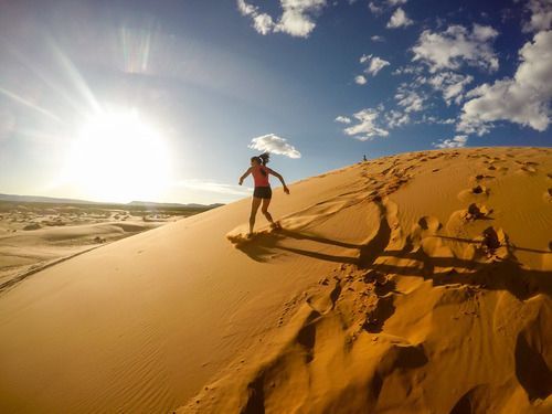 A person runs down a sunlit, golden sand dune under a bright blue sky with scattered clouds.