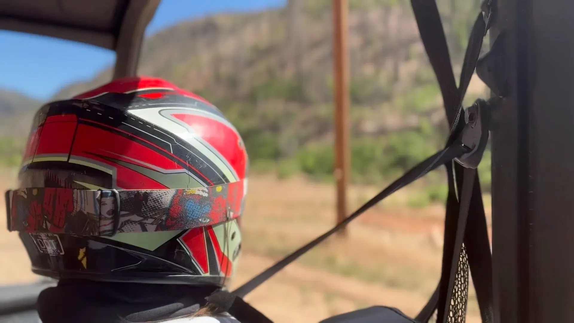 Red and black helmet strapped inside a vehicle, with a blurred roadside view outside.
