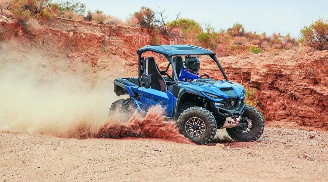 A blue atv is driving down a dirt road in the desert.