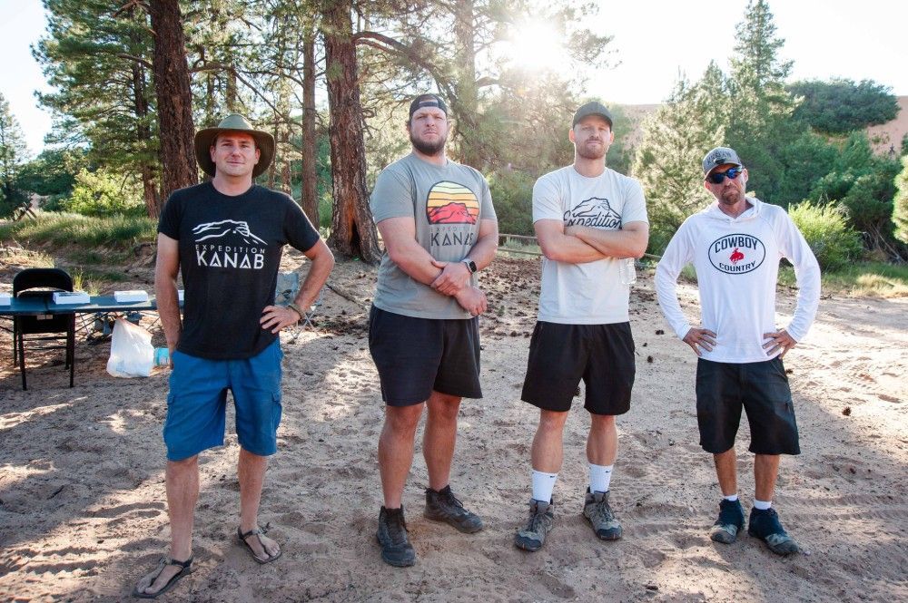 A group of men are standing on a dirt road with their arms crossed.